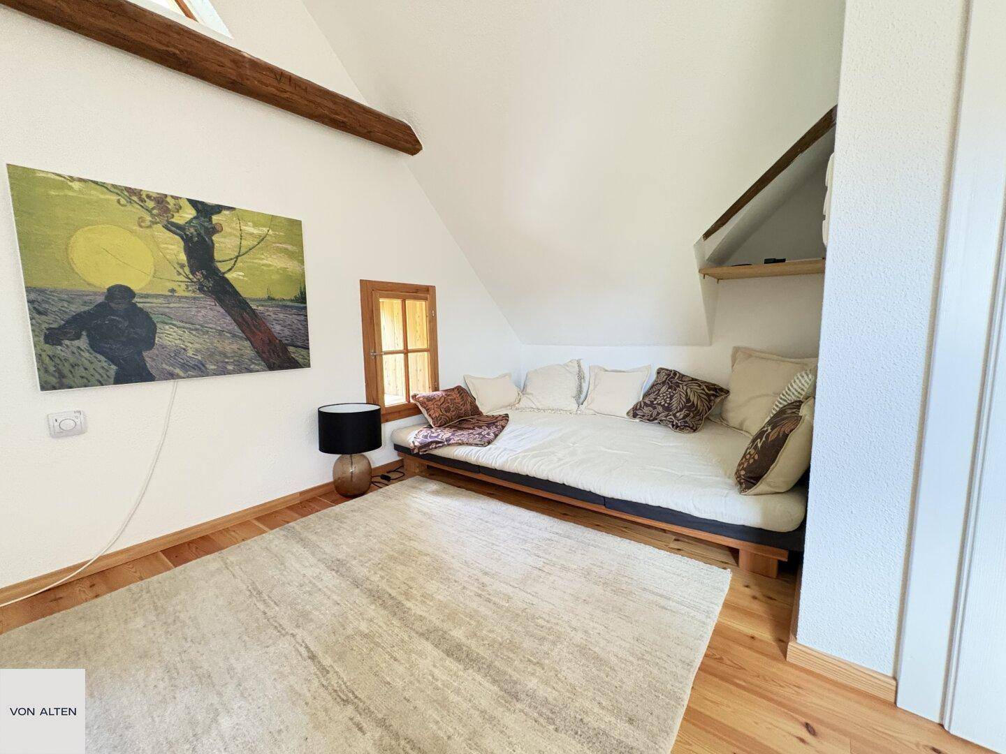 Gemütliches Schlafzimmer im Dachgeschoss mit niedrigem Bett, Holzbalken und einem kleinen Fenster.