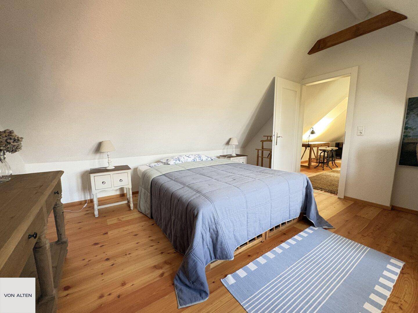 Geräumiges Schlafzimmer im Dachgeschoss mit Doppelbett, Nachttischen und Zugang zu einem weiteren Raum.