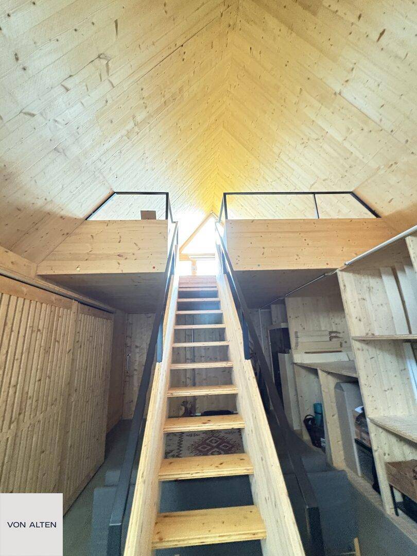 Holzverkleideter Dachboden mit steiler Holztreppe und zwei erhöhten Schlafbereichen.