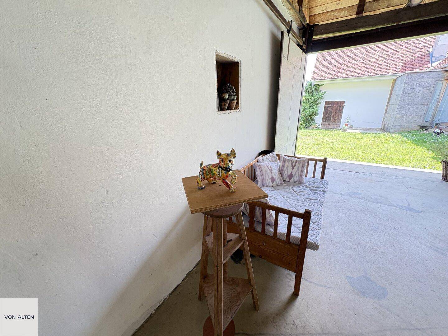 Überdachter Außenbereich mit Holztagesbett und einem kleinen Tisch, ideal zum Entspannen.
