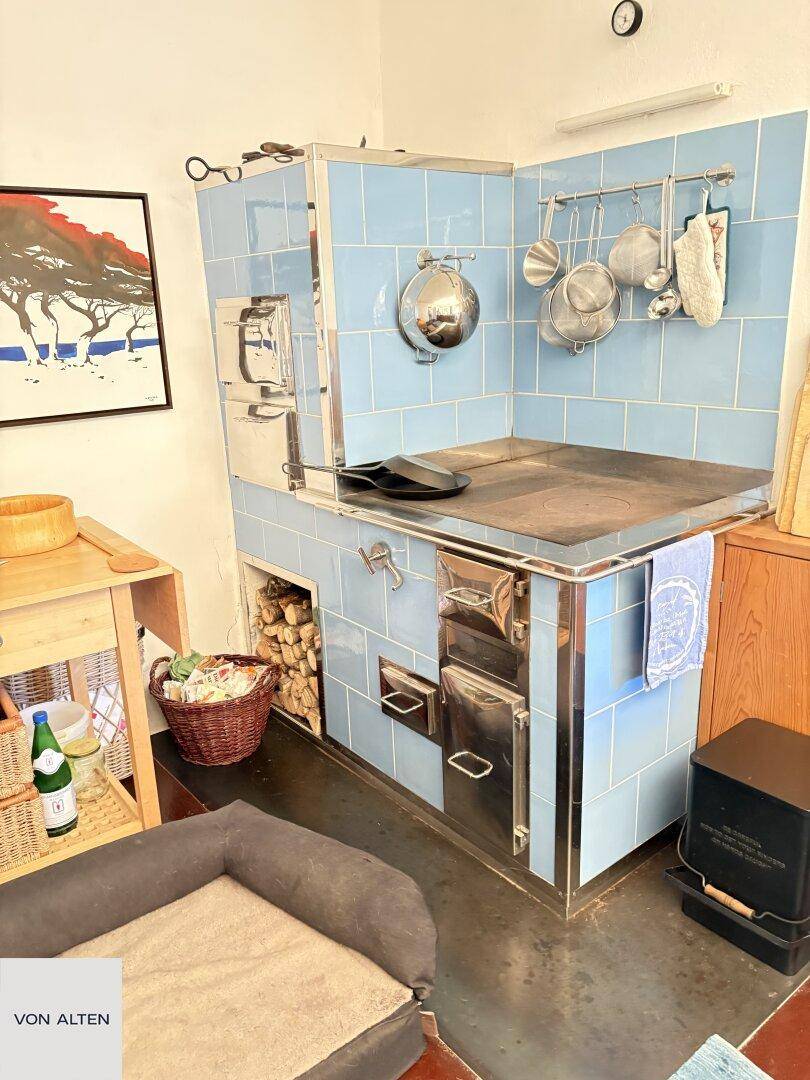 Detailansicht eines traditionellen blauen Kachelofens mit Kochfeld und Holzfach in der Küche.