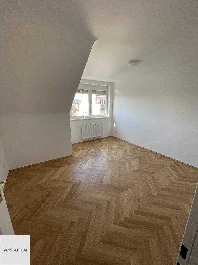 Gemütliches Zimmer mit Fischgrätparkett und Fenster, das viel Tageslicht hereinlässt.