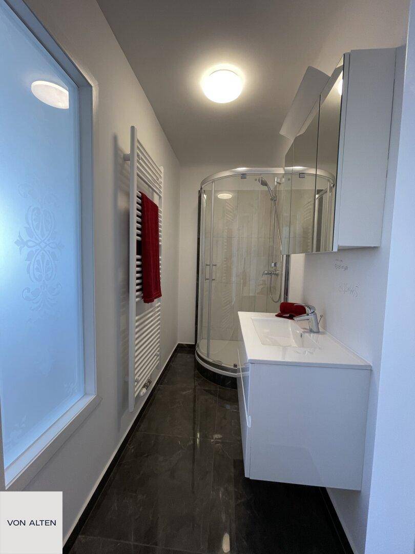 Modernes Badezimmer mit dunklen Fliesen, Duschkabine, Einzelwaschbecken und beheiztem Handtuchhalter.