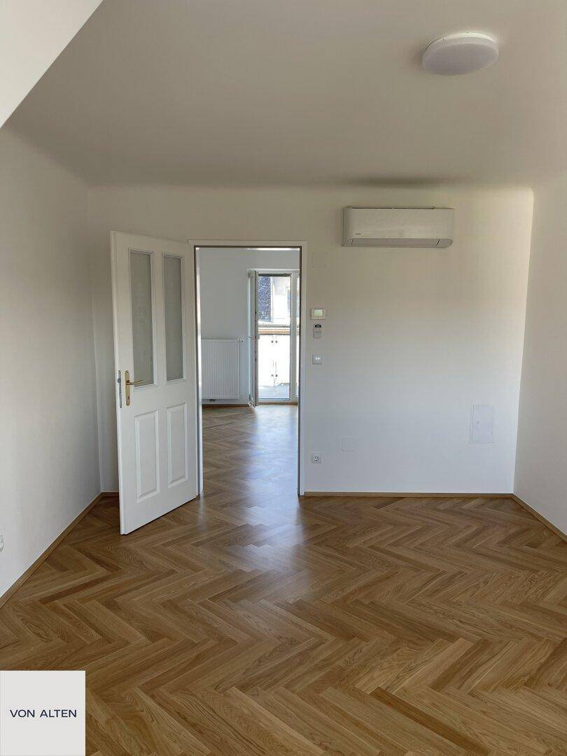 Helles Zimmer mit Fischgrätparkett und Klimaanlage, verbunden mit einem weiteren Raum.