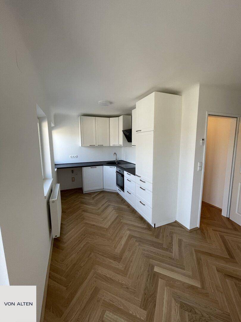 Funktionale Küche mit weißen Schränken, dunkler Arbeitsplatte und Fischgrätparkettboden.