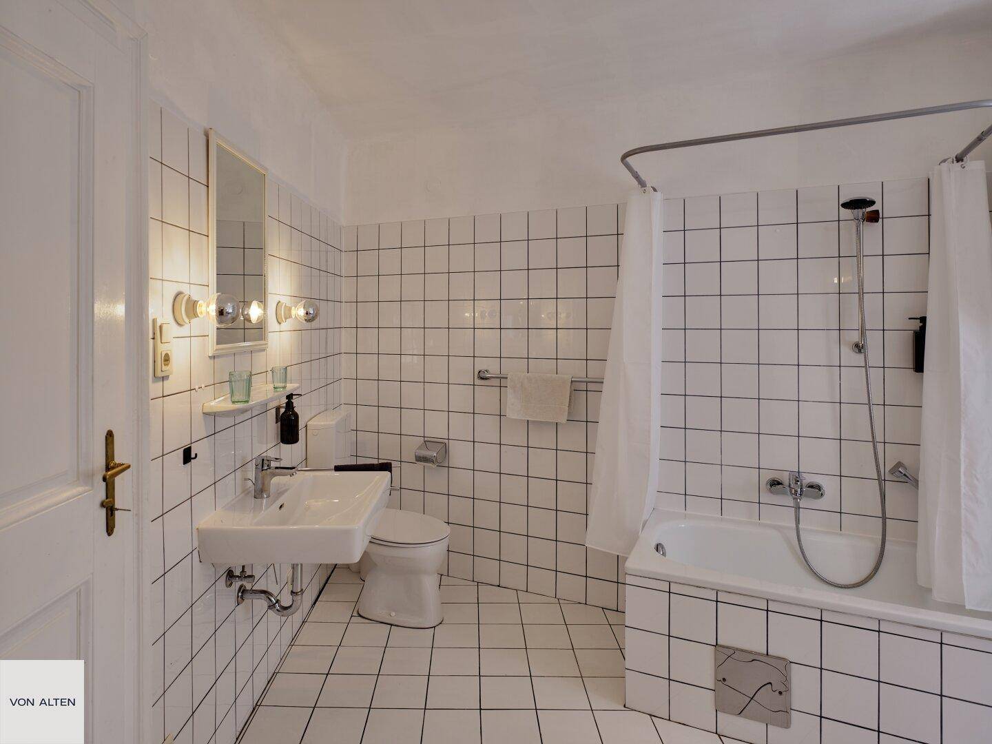 Helles Badezimmer mit weißen Fliesen, Badewanne und Duschvorhang in klassischem Stil.