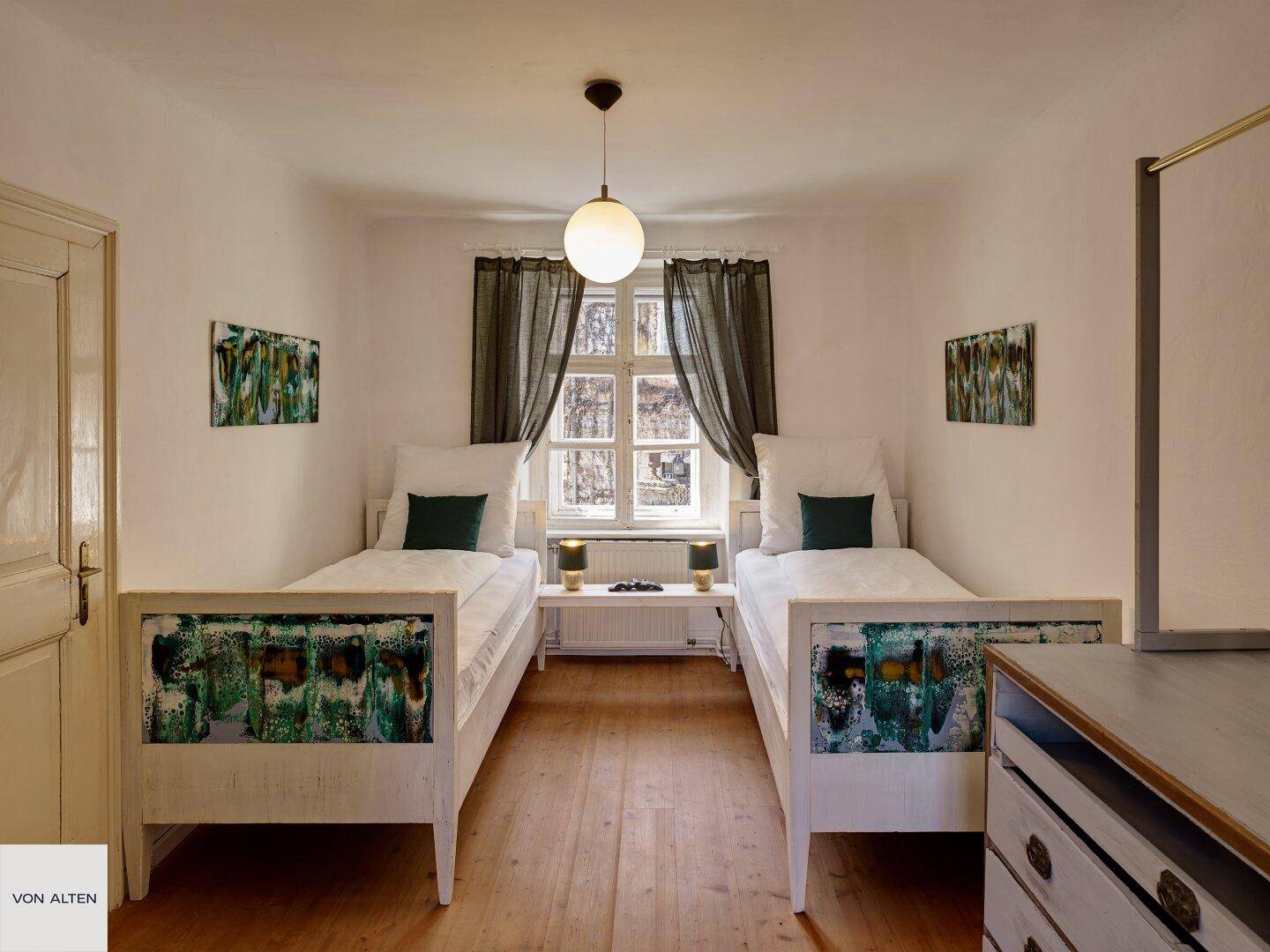 Gemütliches Schlafzimmer mit zwei Einzelbetten, Holzboden und Fenster mit Blick ins Grüne.