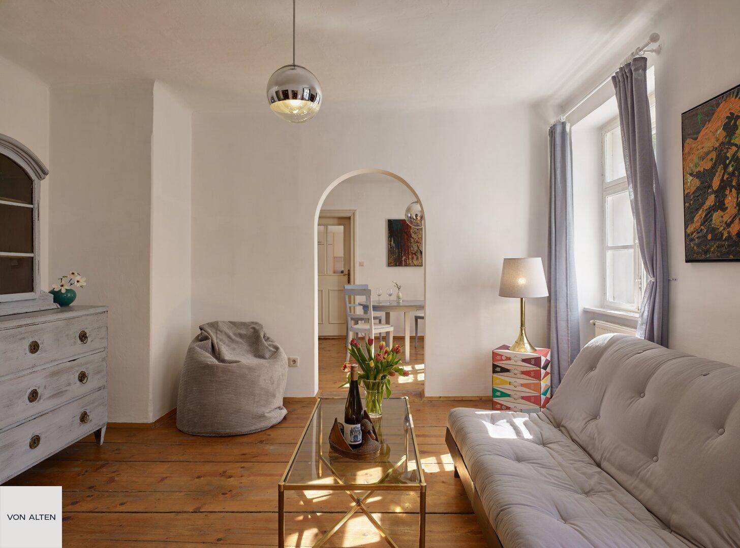Gemütliches Wohnzimmer mit Holzboden, Sofa und einem Durchgang zum Essbereich.