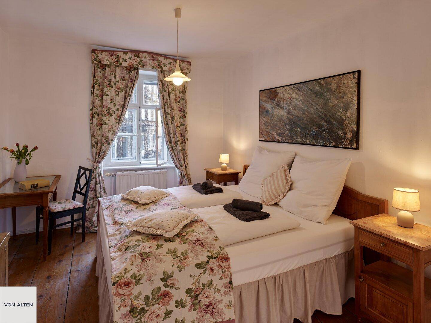 Charmantes Schlafzimmer mit floraler Dekoration, zwei Betten und Holzboden.