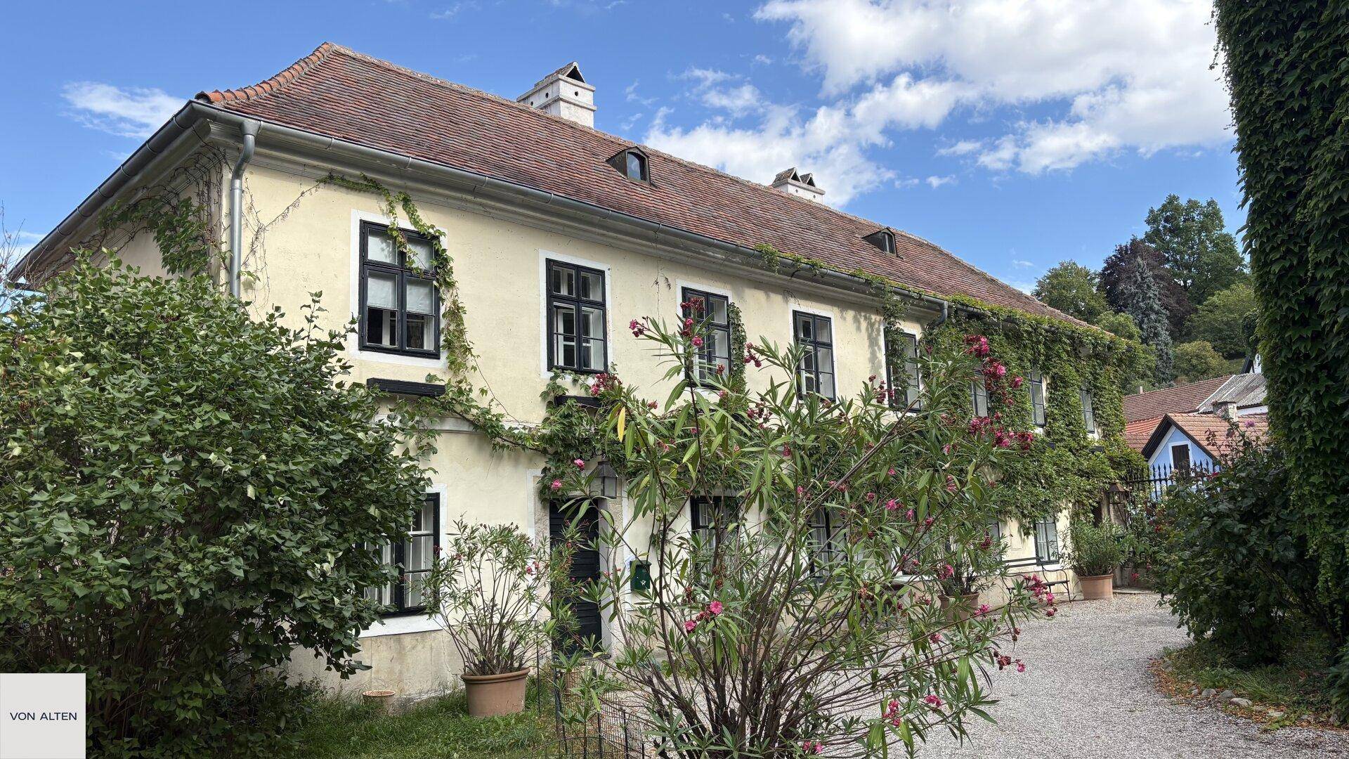 Charmantes historisches Gebäude mit gelber Fassade, roten Dachziegeln und üppiger Bepflanzung.