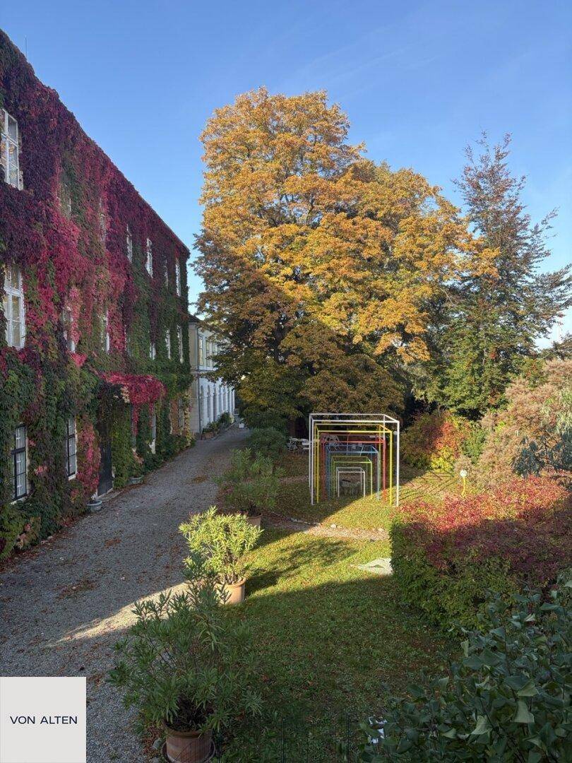 Herbstliche Ansicht des historischen Gebäudes mit farbenprächtigen Bäumen und Gartenbereich.