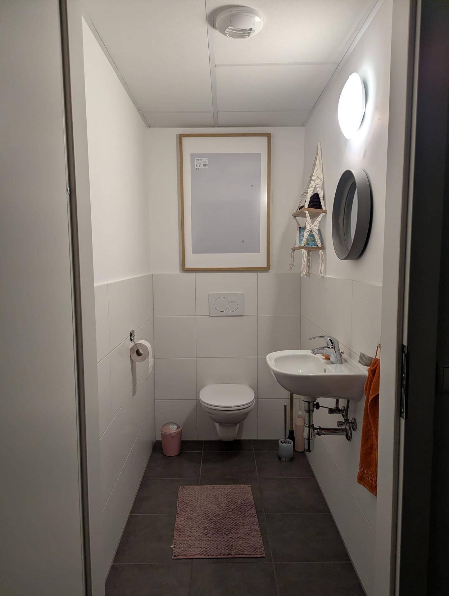 Separates WC mit wandhängender Toilette und kleinem Waschbecken.