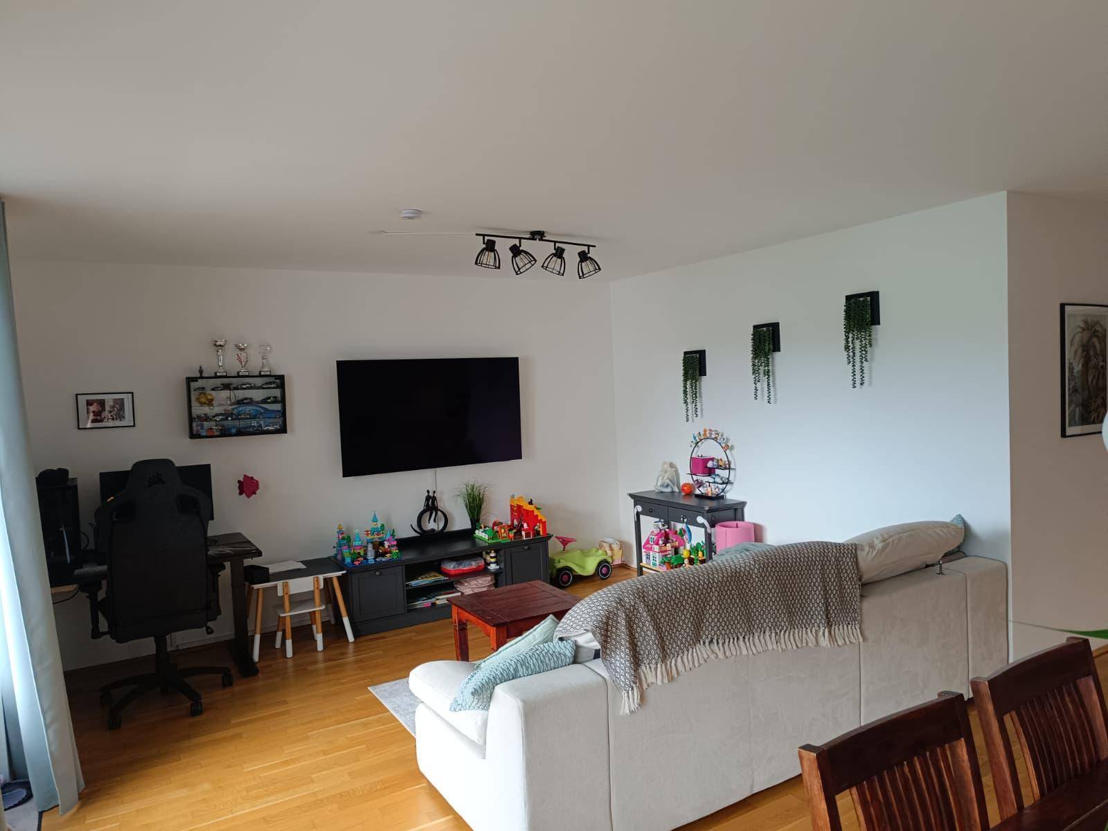 Geräumiges Wohnzimmer mit Fernseher, Schreibtisch und Spielzeug, angrenzend an den Essbereich.