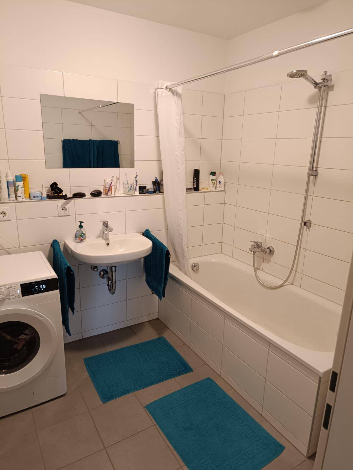 Badezimmer mit Badewanne, Waschbecken und Waschmaschine, ausgestattet mit weißen Fliesen.