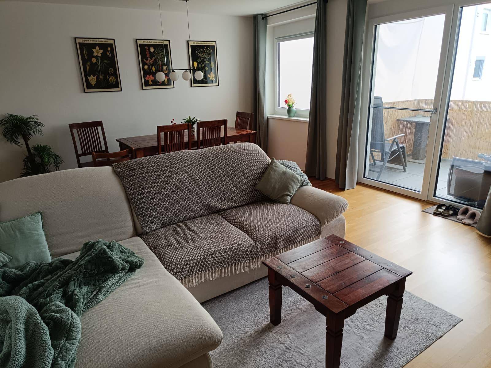 Heller Wohn- und Essbereich mit Zugang zu einem Balkon, ausgestattet mit einem bequemen Sofa und Esstisch.