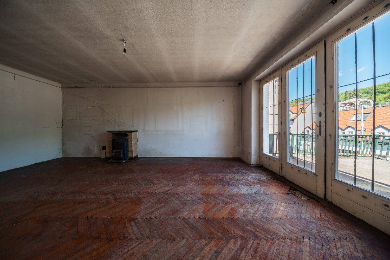 Geräumiges Wohnzimmer mit Fischgrätparkett, großen Fenstern und Zugang zur Terrasse.