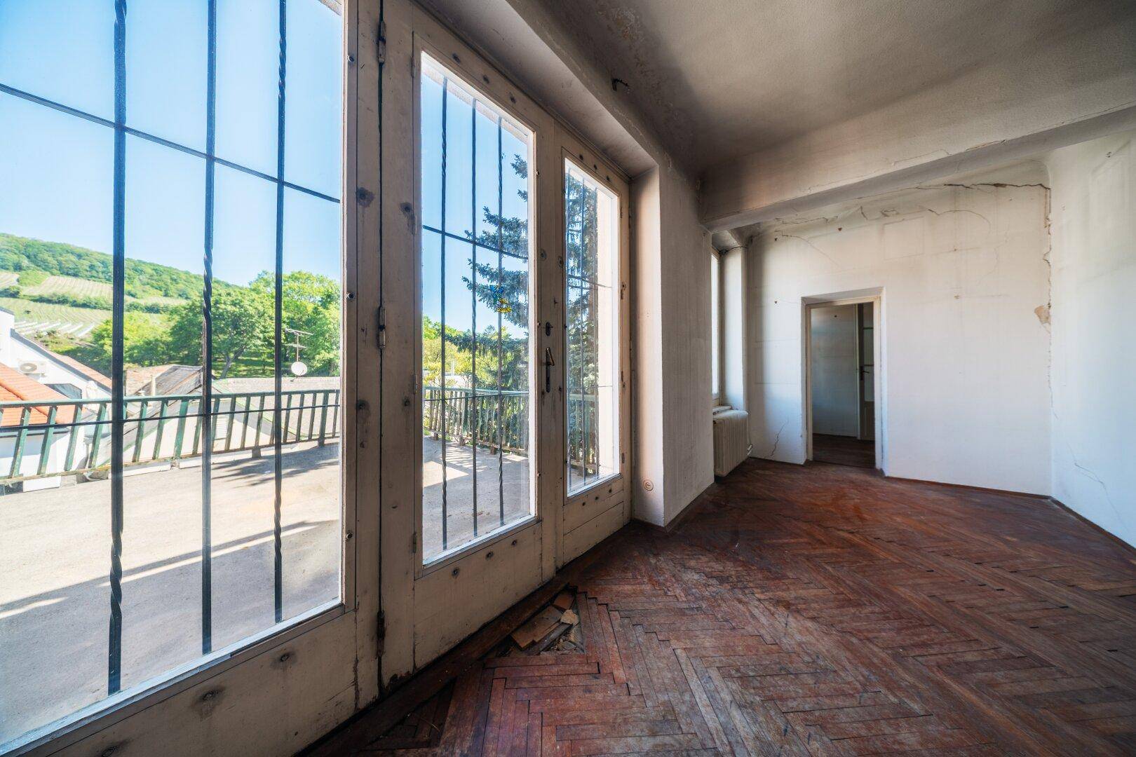 Helles Zimmer mit Parkettboden und großen Fenstertüren, die auf eine Außenterrasse führen.
