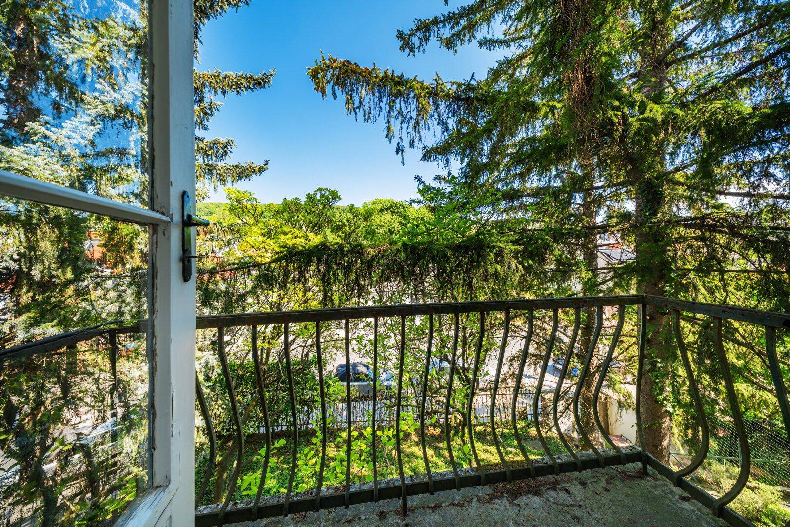 Kleiner Balkon mit schmiedeeisernem Geländer und Blick auf Bäume und die Straße.