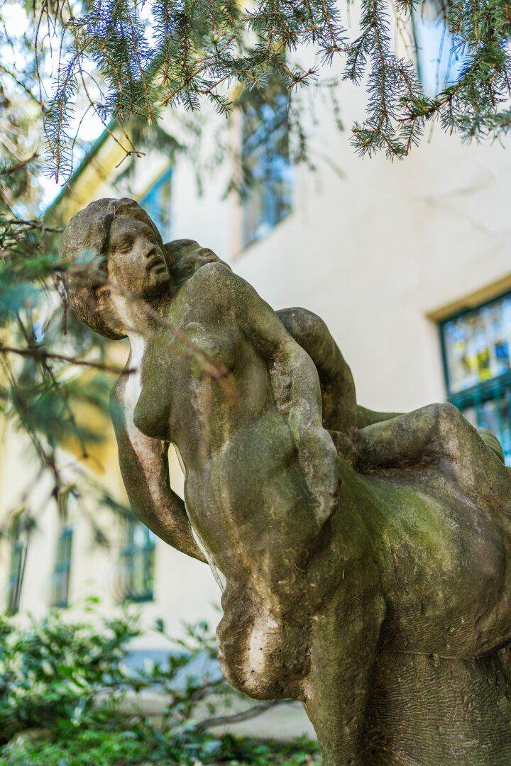 Detailansicht einer alten Steinstatue mit Moosbewuchs vor einem Gebäude.
