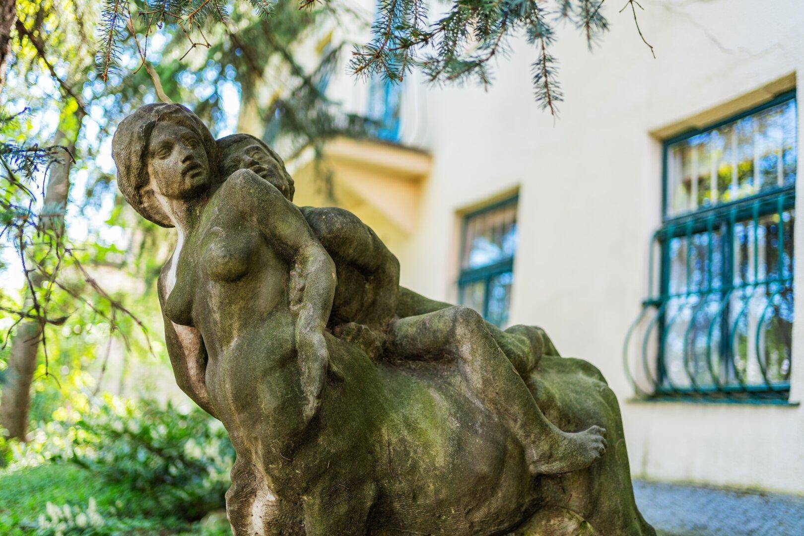 Antike Steinstatue mit Moosbewuchs vor der Fassade eines historischen Gebäudes.
