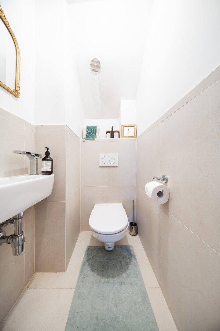 Kleines Gäste-WC mit Wand-WC, Waschbecken und hellen Fliesen.