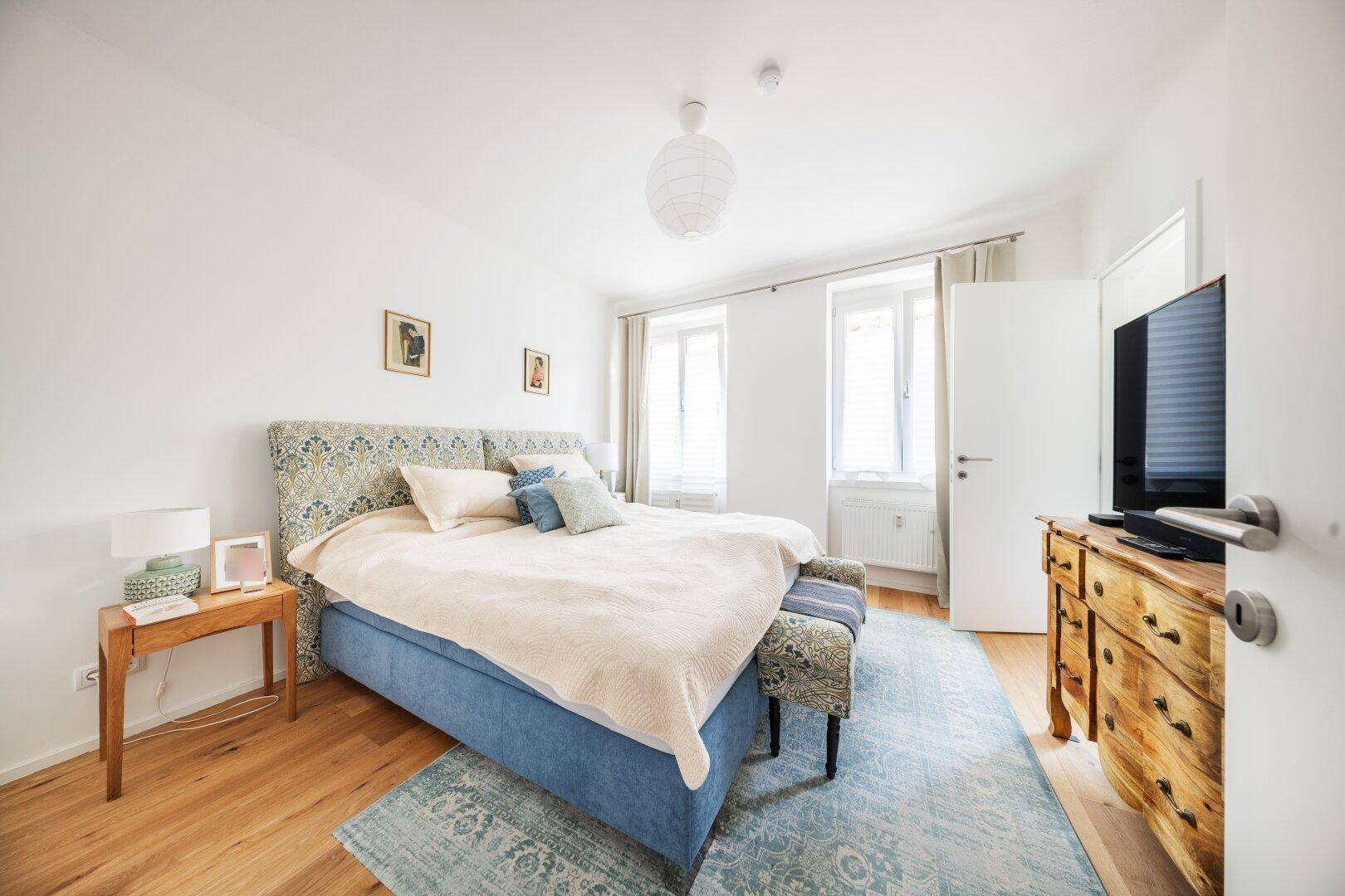 Gemütliches Schlafzimmer mit Holzboden, großem Bett und einem Teppich in Blautönen.