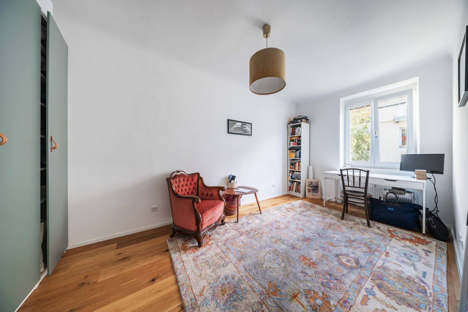 Arbeitszimmer mit Holzboden, einem roten Sessel, Schreibtisch und Bücherregal.