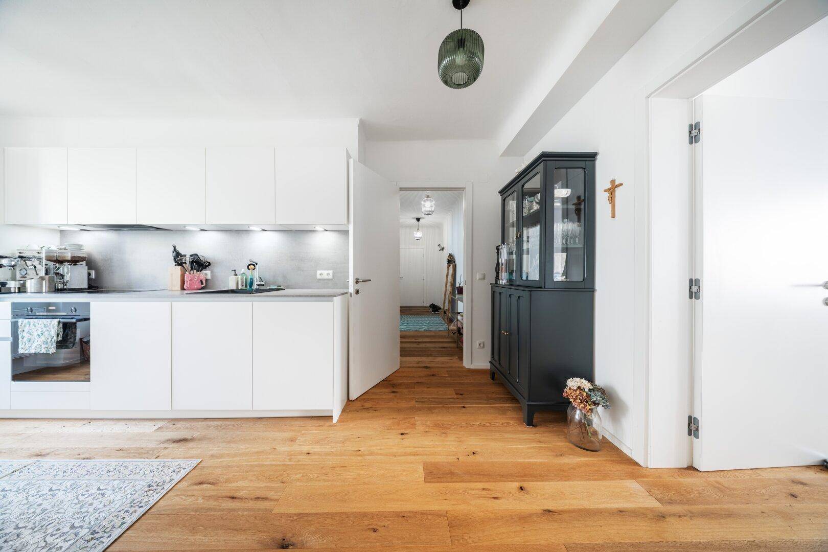 Moderne Küche mit weißen Fronten und Holzboden, offen zum Flur.