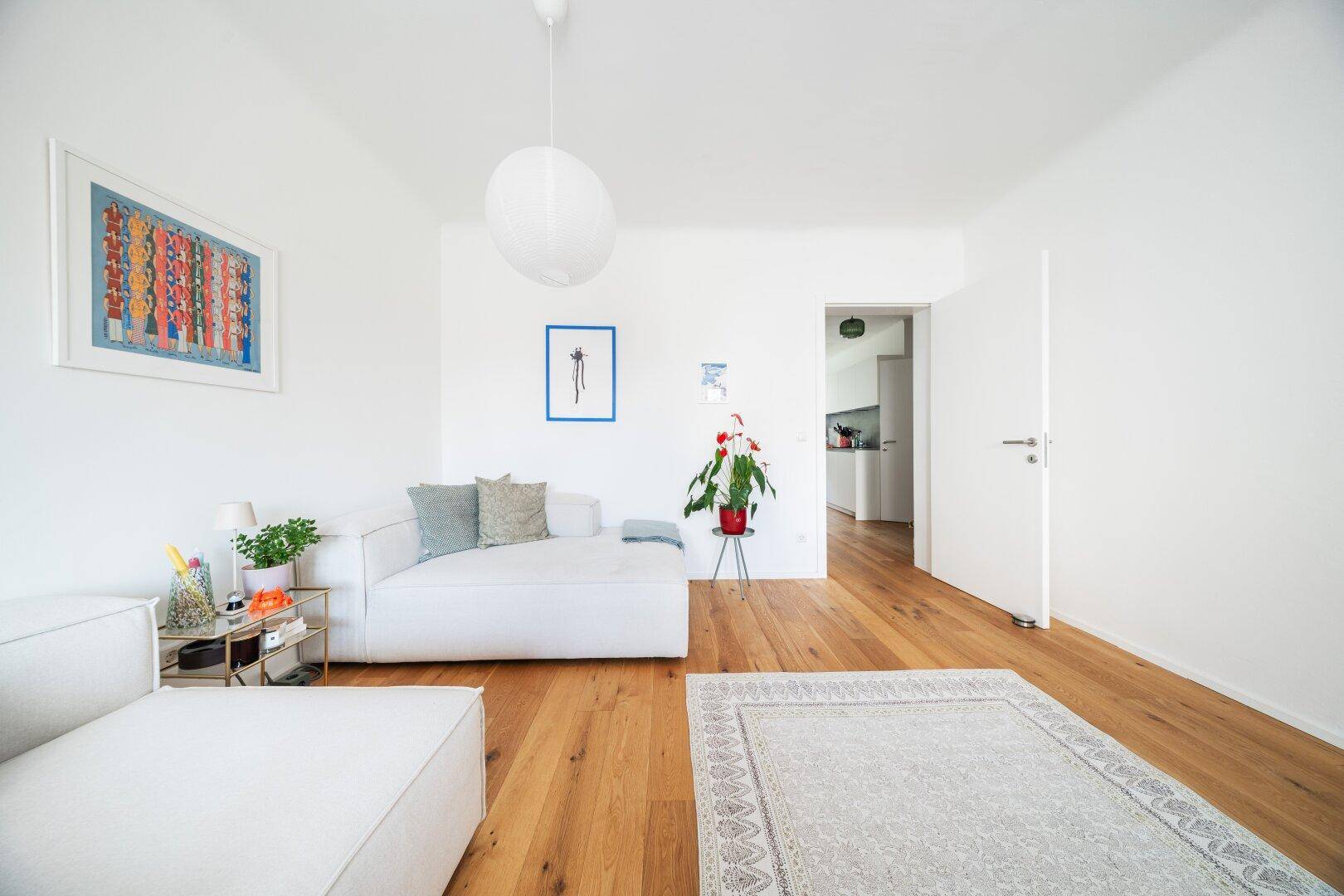 Heller Wohnbereich mit Holzboden, modernen Sofas und Blick in die Küche.