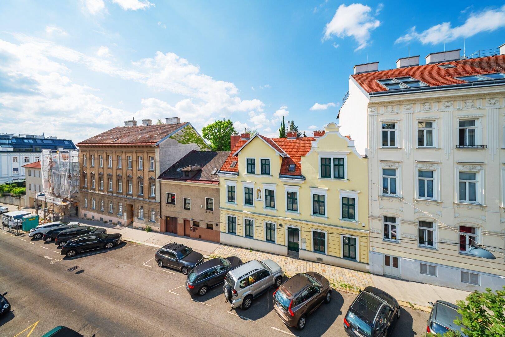 Blick auf eine belebte Straße mit parkenden Autos und historischen Gebäuden.