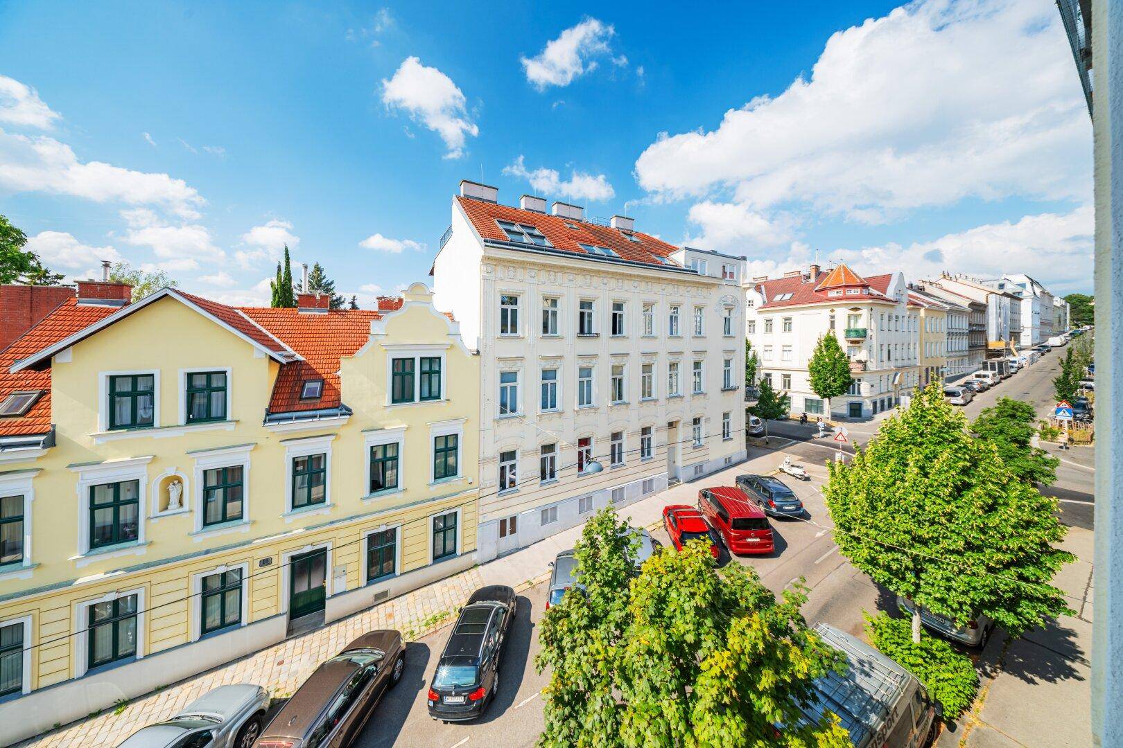 Panoramablick auf eine städtische Straße mit Gebäuden und parkenden Fahrzeugen unter blauem Himmel.