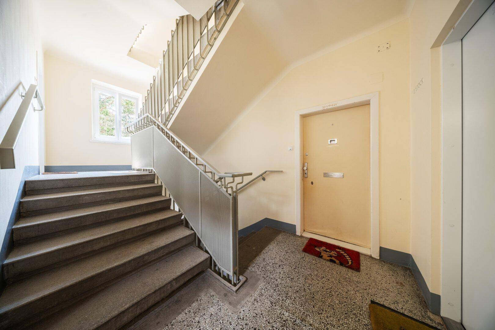 Treppenhaus mit Terrazzoboden, Metallgeländer und Zugang zu den Wohnungen.