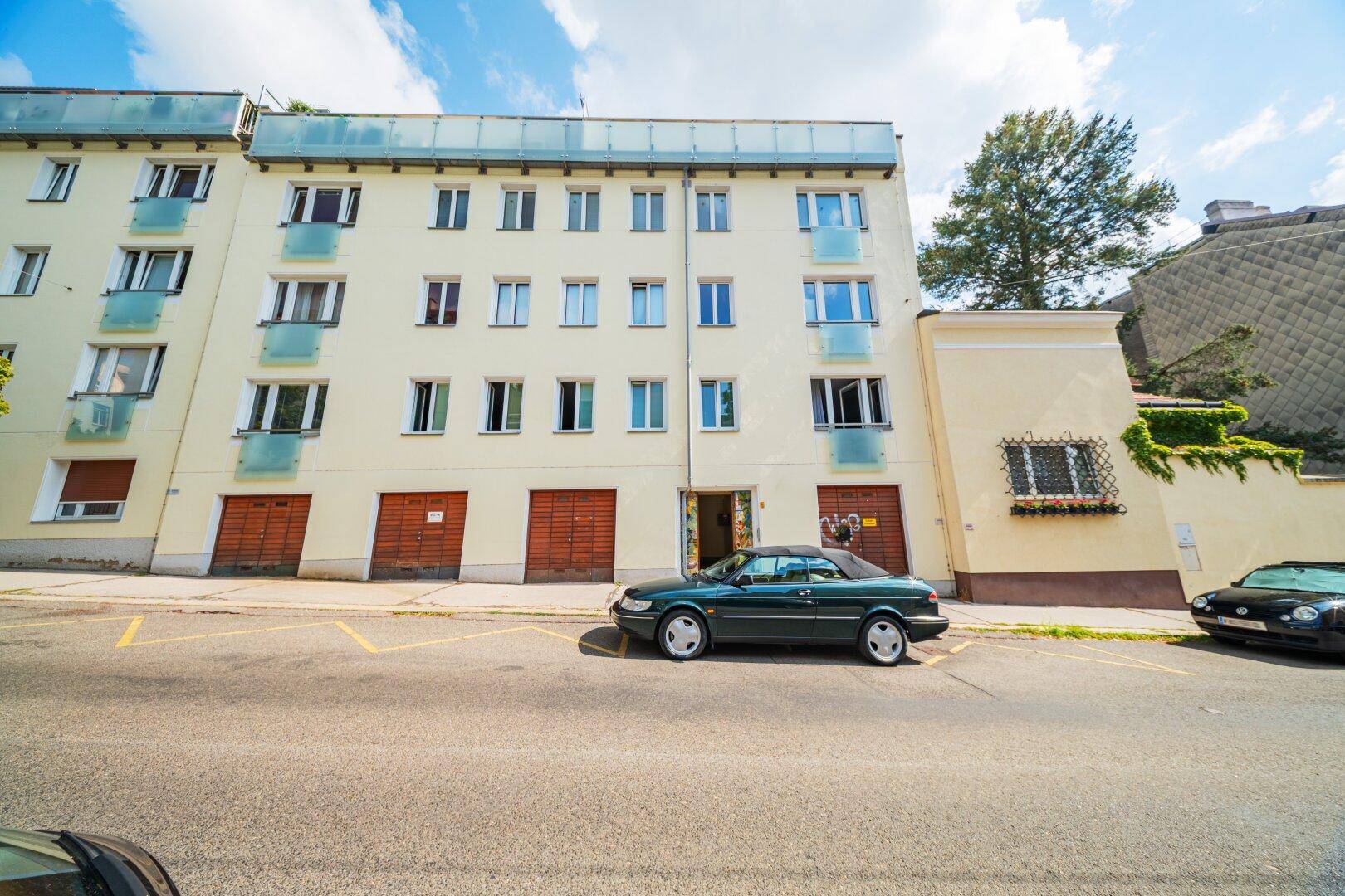 Fassade eines Mehrfamilienhauses mit Balkonen und Garagentoren an der Straßenseite.