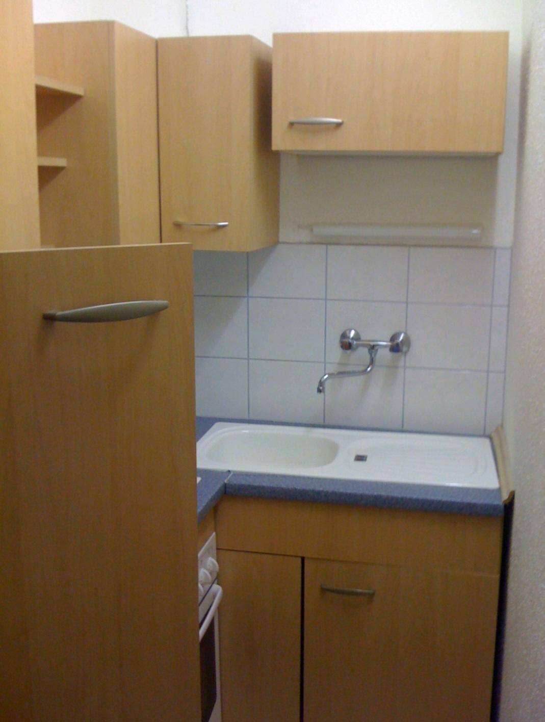 Kleine Küche mit Holzschränken, Doppelspülbecken und weißem Fliesenspiegel an der Wand.