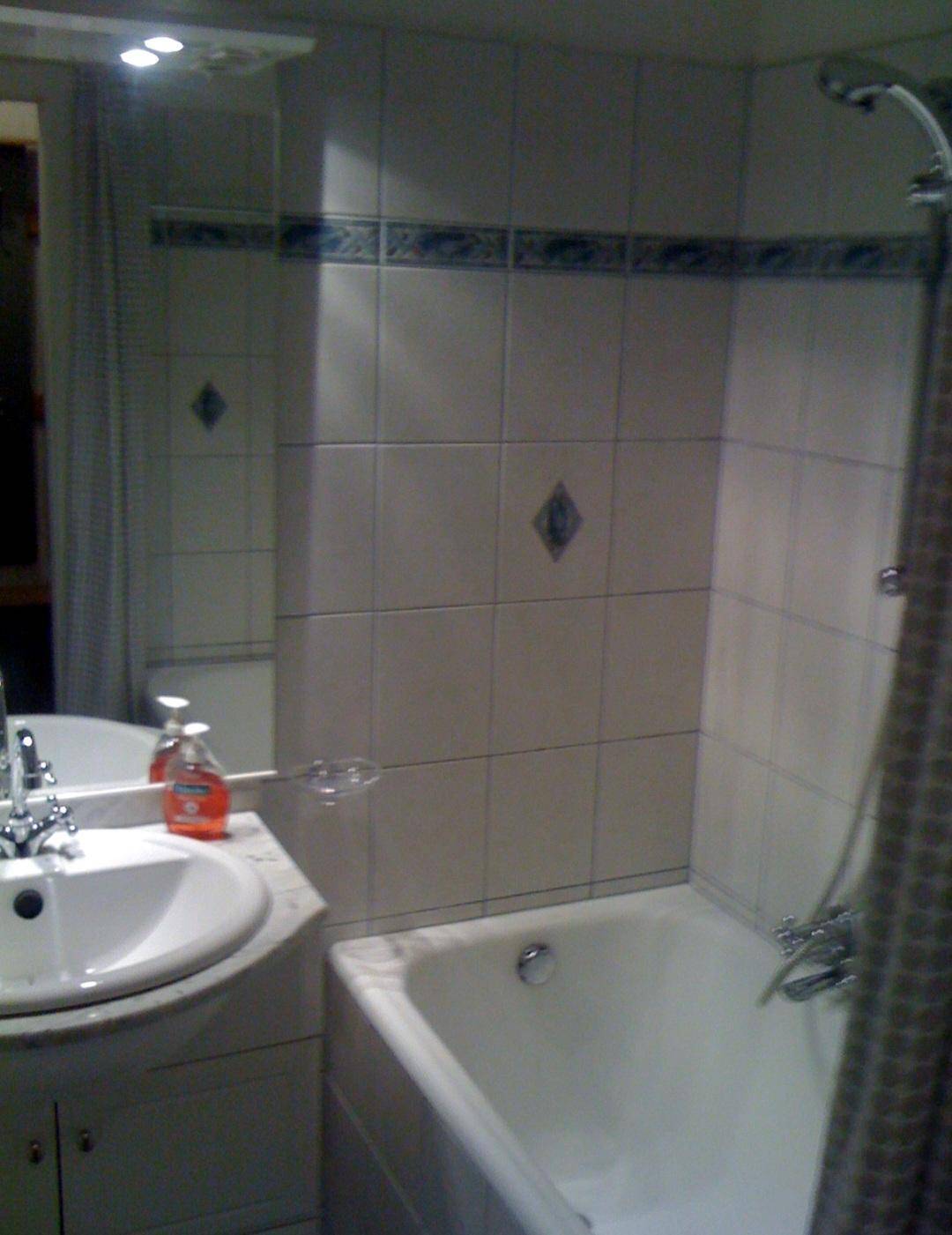 Badezimmer mit Badewanne, Dusche, Waschbecken und hellen Fliesen im Stil der 80er Jahre.