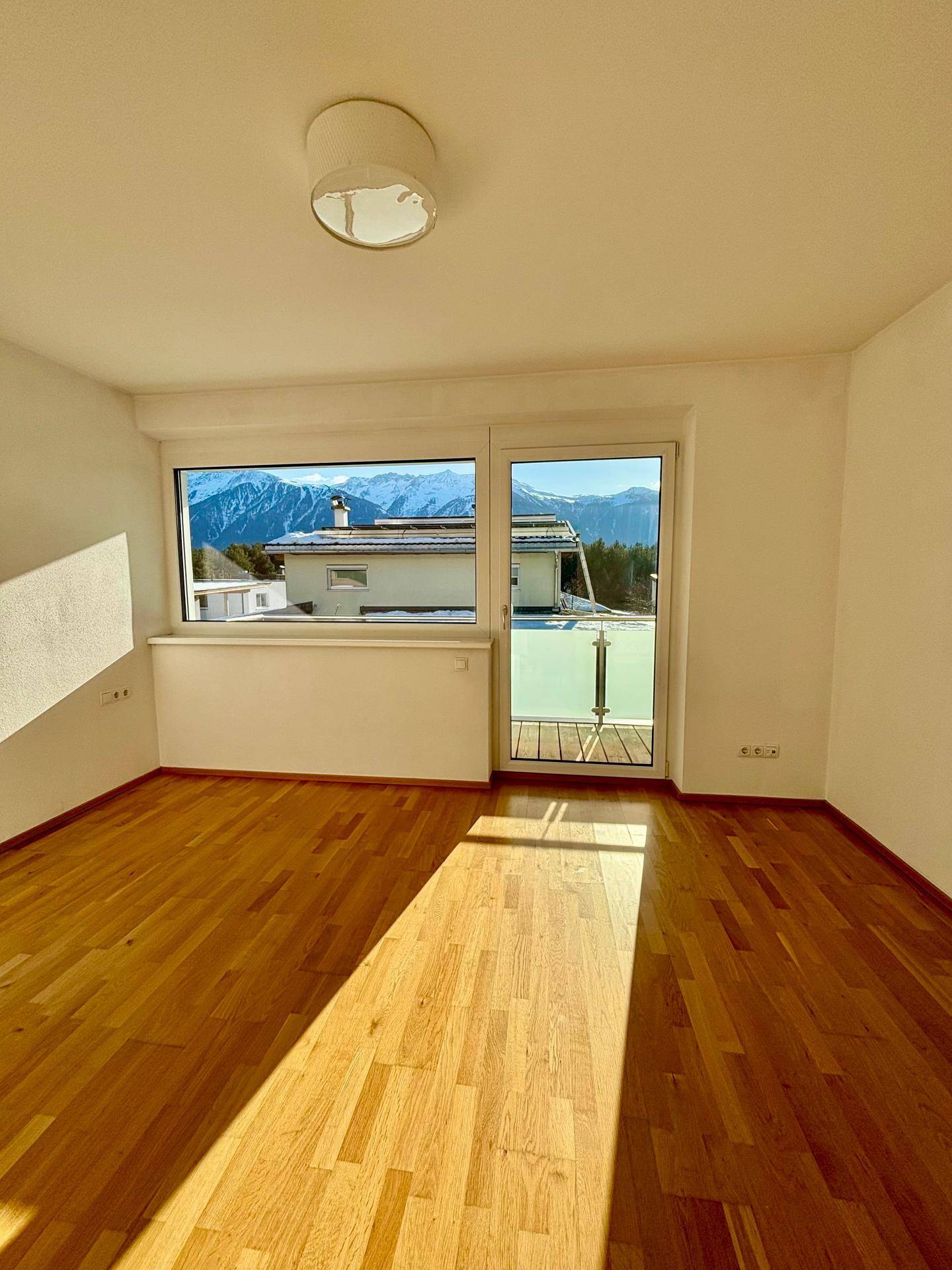 Helles Schlafzimmer mit Holzboden, Balkonzugang und Bergblick.