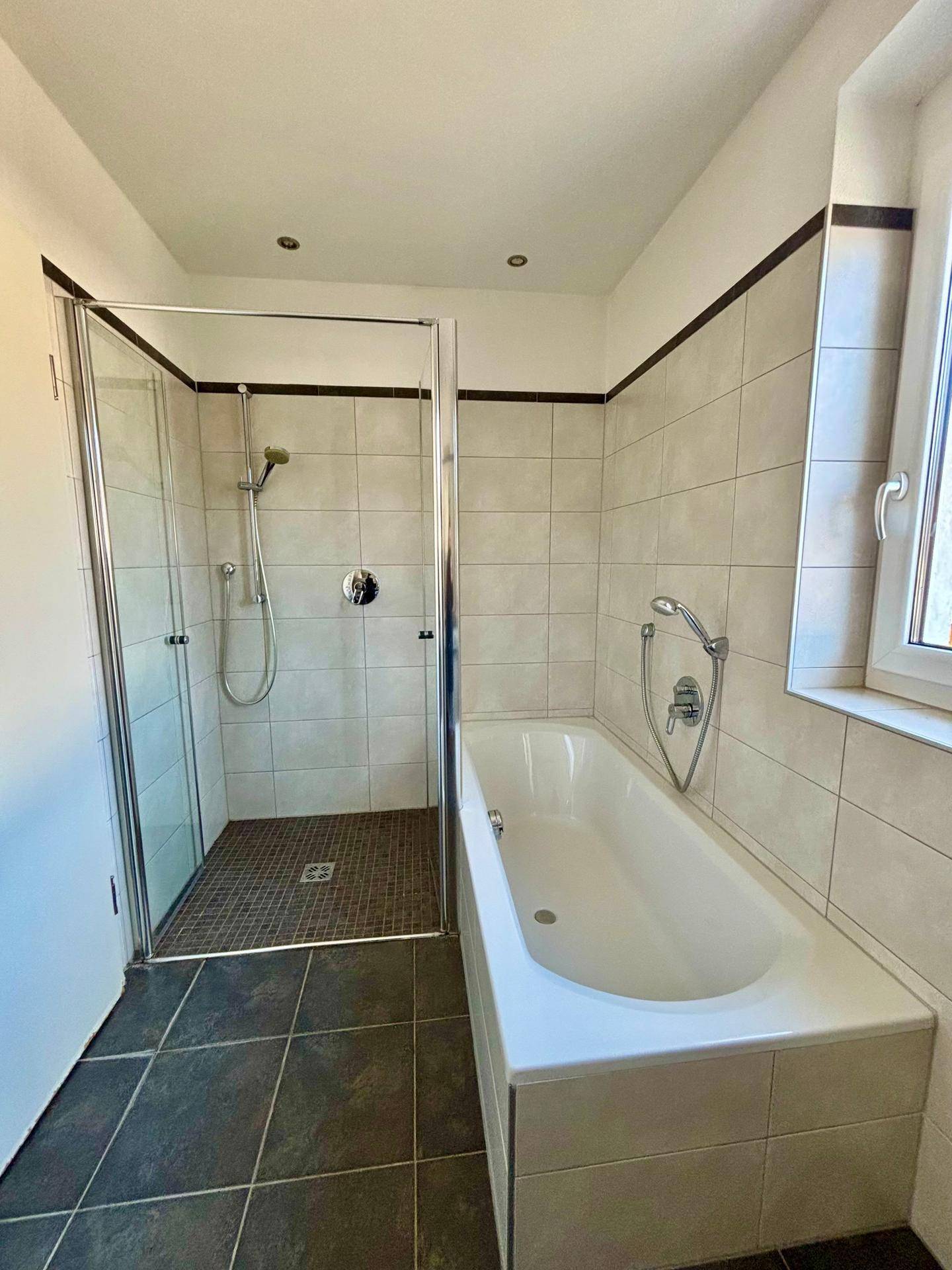 Helles Badezimmer mit Badewanne, Duschkabine und Fenster.