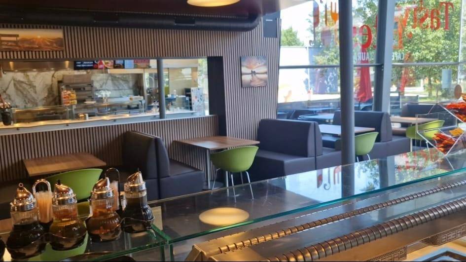 Innenansicht eines modernen Restaurants mit bequemen Sitzbänken, Tischen und Blick auf die offene Küche.