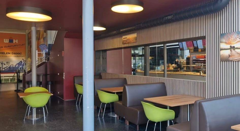 Gemütlicher Restaurantbereich mit modernen Sitzbänken, hellgrünen Stühlen und Blick auf eine Treppe im Hintergrund.