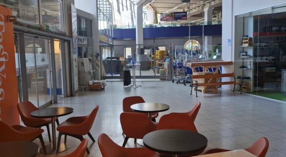 Geräumiger, heller Gewerberaum mit hohen Decken, Glasfronten und einem kleinen Café-Bereich mit modernen Stühlen.