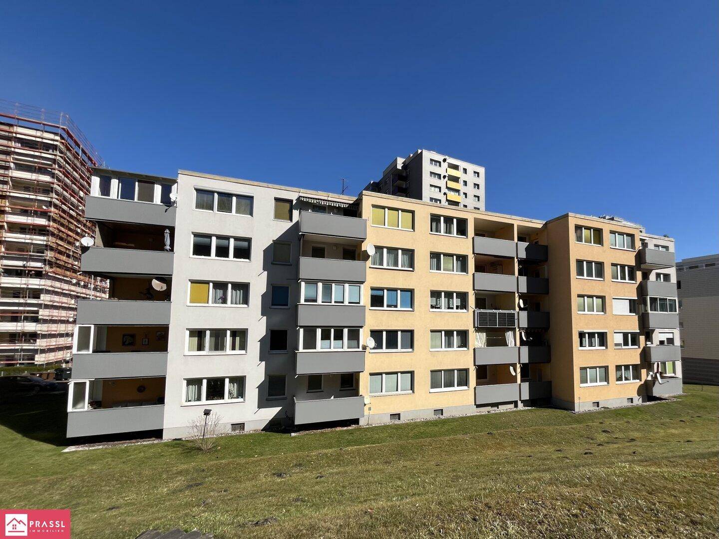 Mehrfamilienhaus mit Balkonen und gelber Fassade in sonniger Umgebung.