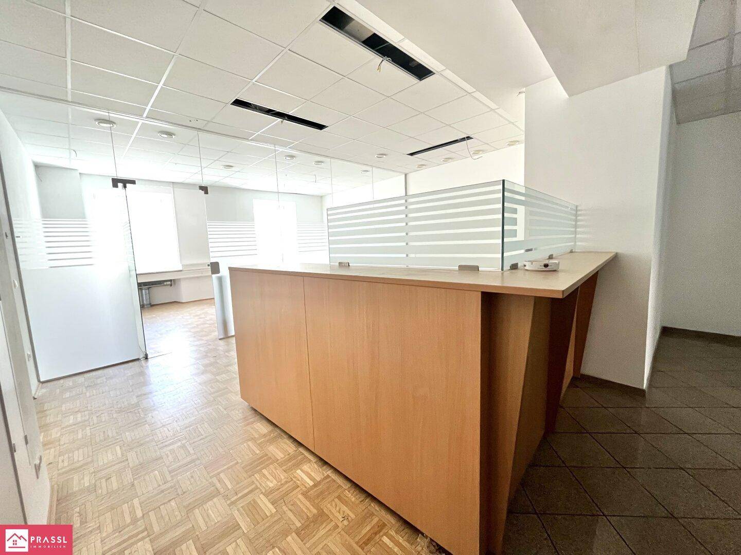 Empfangsbereich eines Büros mit Holztresen, Glasabtrennungen und modularen Deckenplatten.
