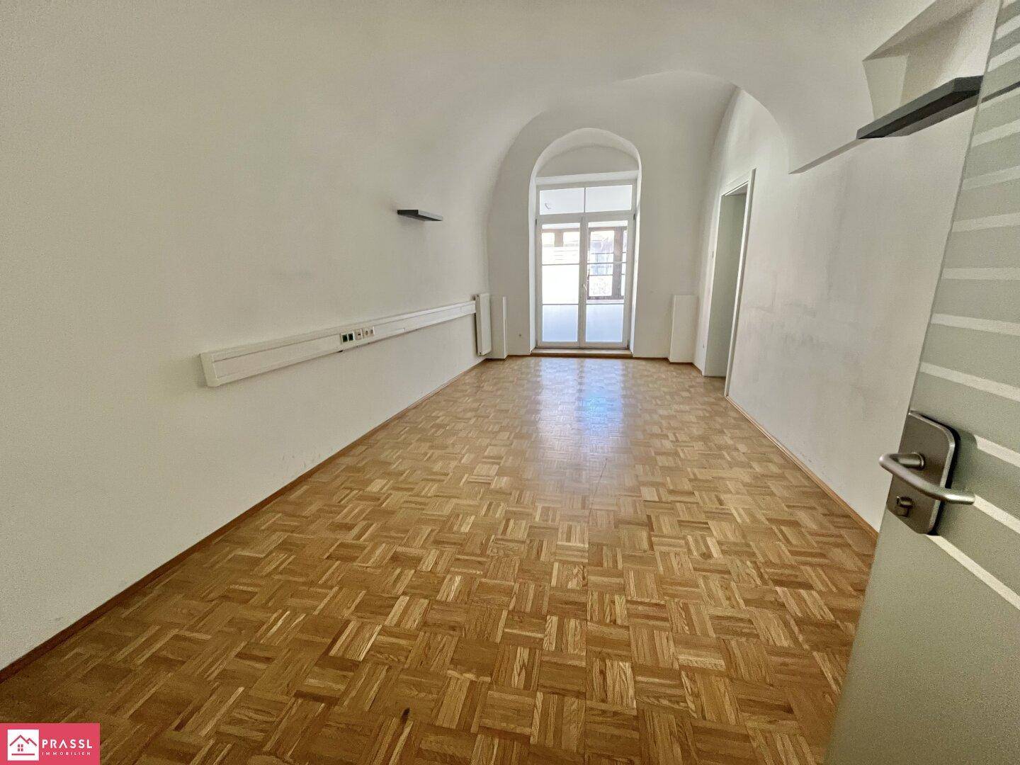 Langer Flur mit Parkettboden, gewölbter Decke und einem großen Bogenfenster am Ende.