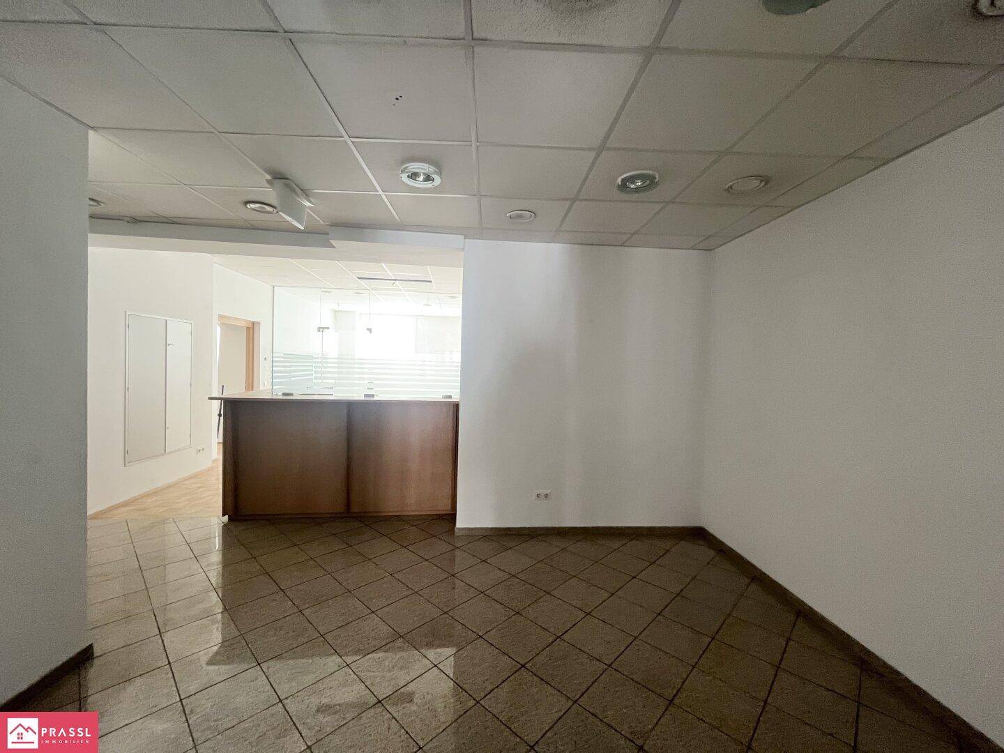 Offener Bürobereich mit Fliesenboden und Blick auf einen Empfangstresen im Hintergrund.
