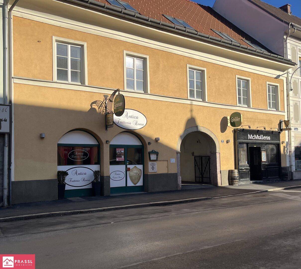 Historisches Gebäude mit Geschäften im Erdgeschoss und traditioneller Architektur in einer städtischen Umgebung.