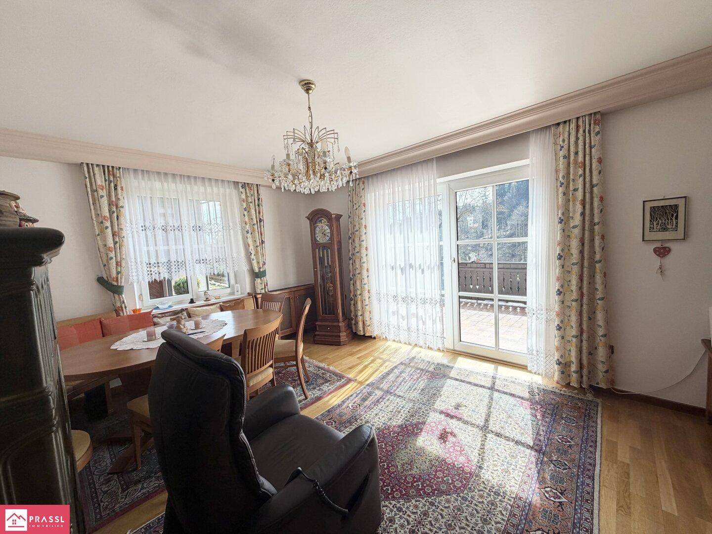 Helles Wohn-Esszimmer mit Holzboden, Kronleuchter und Zugang zu einem sonnigen Balkon.