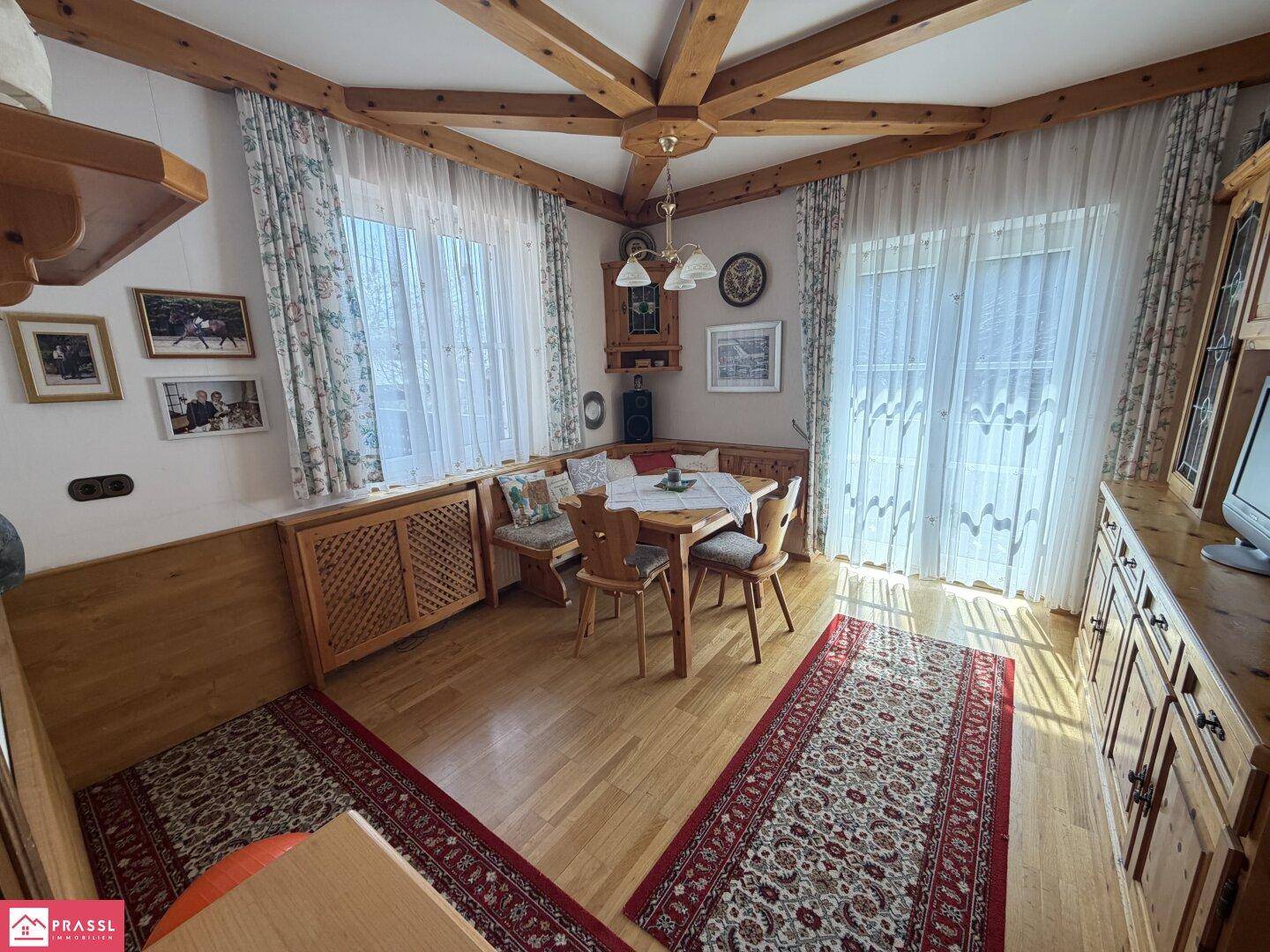 Rustikales Wohnzimmer mit Holzbalkendecke, Holzboden und gemütlichem Essbereich.