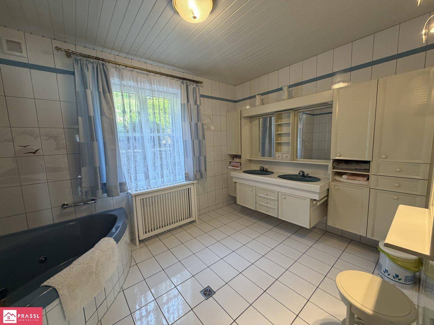 Geräumiges Badezimmer mit blauer Badewanne, Doppelwaschbecken und Fenster.