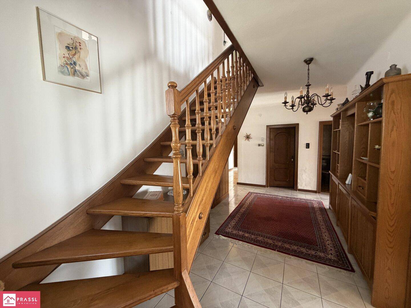 Geräumiger Flur mit Holztreppe, Fliesenboden und traditionellen Holzmöbeln.