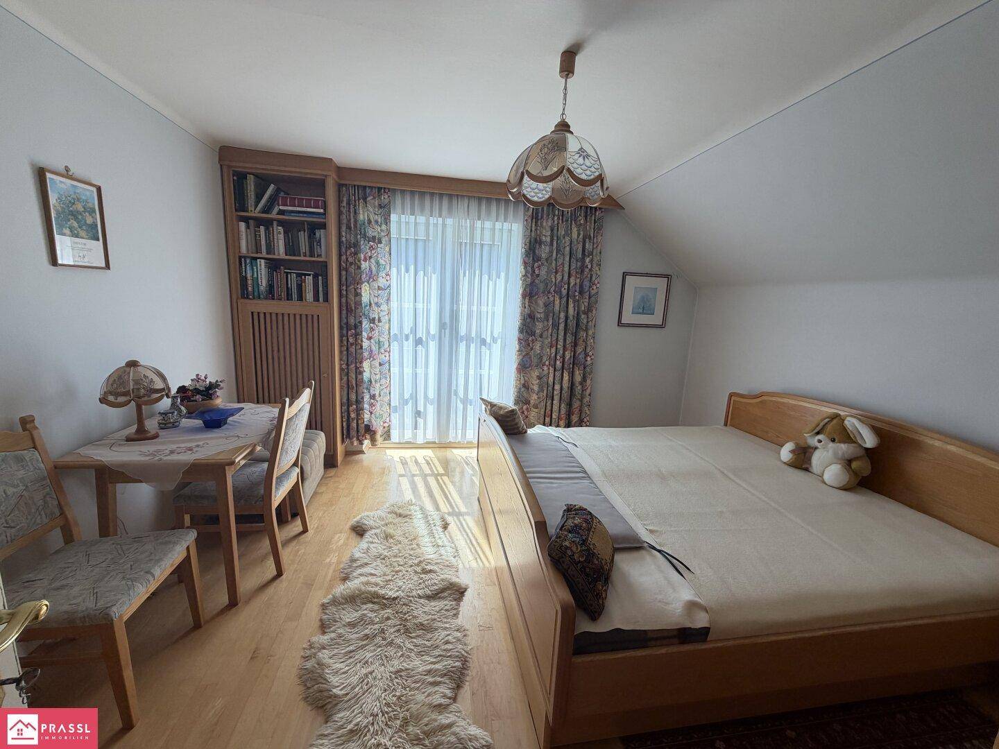 Schlafzimmer im Dachgeschoss mit Holzboden, Bett und Zugang zum Balkon.